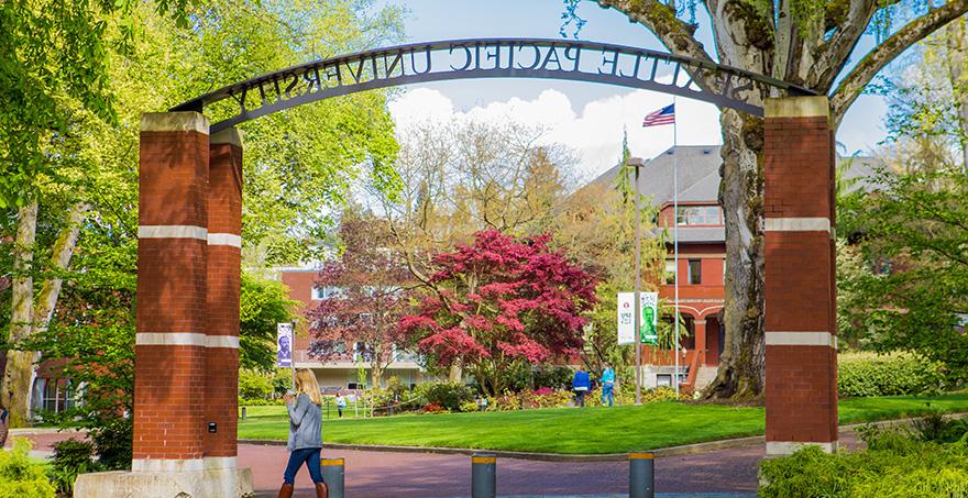 An SPU student walks by the Seattle Pacific University entry archway on a bright spring day